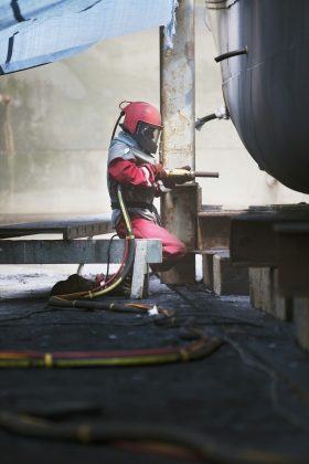 Worker sandblasting boat hull in shipyard